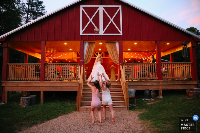Photo by: <a href="https://www.wpja.com/contests/2017-tri2-photography-competition/bouquetgarter-action/2028871">Leah Moyers - United States</a> Knoxville wedding photographer captured this photo of two bridesmaids clamoring for the bouquet as the bride tosses it off the top step of a shelter house painted red and white to look like a barn