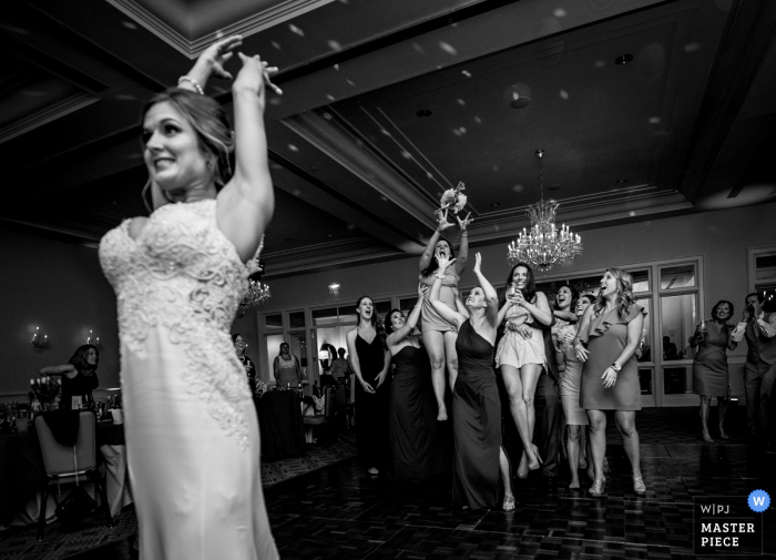 Charlotte wedding photographer captured this black and white photo of the bride tossing her bouquet and the group of women clamoring for it 