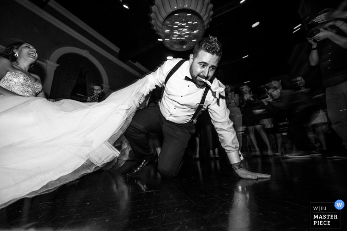Photo by: <a href="https://www.wpja.com/contests/2017-tri2-photography-competition/bouquetgarter-action/2051481">Cafa Liu - Canada</a> Ontario wedding photographer captured this black and white image of the groom on the floor with the garter in his mouth while the bride laughs in a chair next to him