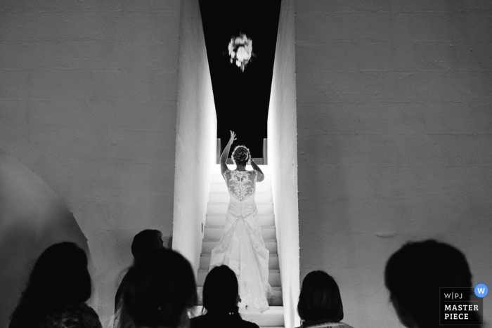 Taranto wedding photographer captured this black and white image of a bride standing on an all white staircase looking towards a night sky while tossing her bouquet behind her