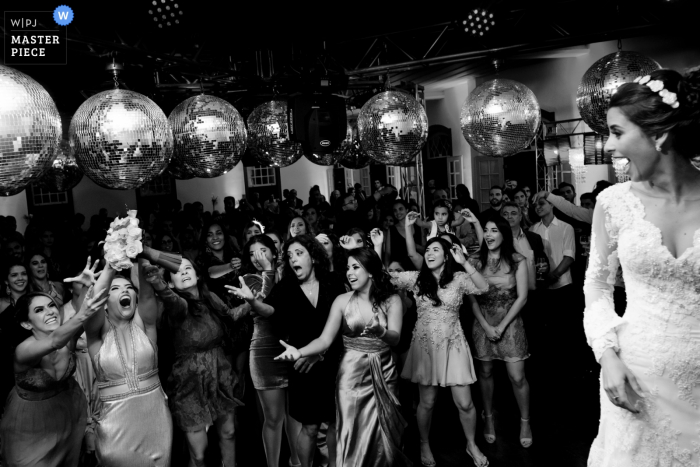 O fotógrafo de casamento no Brasil capturou esta imagem em preto e branco dos convidados do casamento clamando pelo buquê enquanto bolas de discoteca penduradas acima