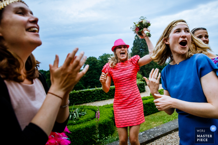 Fotograf ślubny z Flandrii uchwycił to zdjęcie gościa weselnego świętującego złapanie bukietu w ogrodzie otoczonym żywopłotem