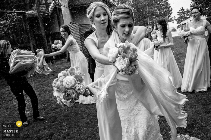 A bridesmaid helps the bride protect her dress from the elements in a photo captured by a Lake Tahoe wedding photographer