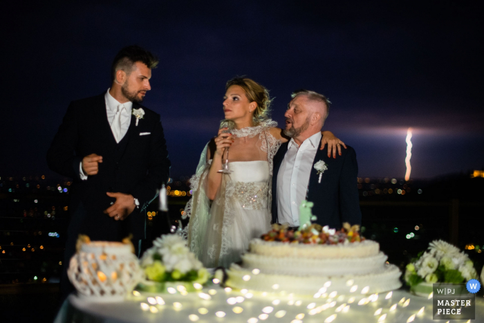 Foto por: <a href="https://www.wpja.com/contests/2017-tri2-photography-competition/weather/2019546"> Alessandro Di Noia - Italia </a> El fotógrafo de bodas de Brescia capturó a estos novios de pie frente a su pastel mientras un rayo de luz golpea en el cielo nocturno en la distancia.