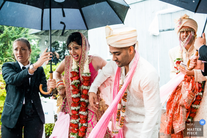 Atlantic City wedding photographer captured this image of a bride and groom laughing under umbrellas as they get caught in a rainstorm during their ceremony