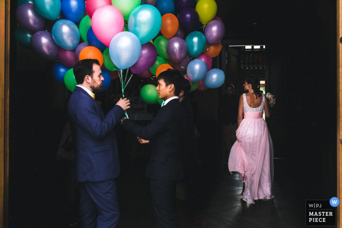 Photo by: <a href="https://www.wpja.com/contests/2017-tri2-photography-competition/flowersdecorations/2021976">Marine Poron - France</a> A groom holds a huge cluster of balloons as a bridesmaid walks by in this image as captured by a Paris wedding photographer