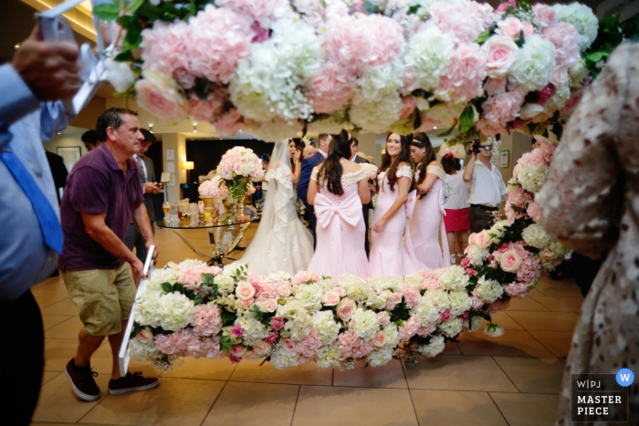 Photo by: <a href="https://www.wpja.com/contests/2017-tri2-photography-competition/flowersdecorations/2041236">Anna Mikulich - United Kingdom</a> Hampshire wedding photographer captured this photo of bridesmaids clustered in pink dresses waiting for the florist to finish setting up the flowered covered arch