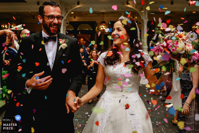 Photo by: <a href="https://www.wpja.com/contests/2017-tri2-photography-competition/flowersdecorations/2045961">Rahul Khona - United Kingdom</a> The image of the bride and groom holding hands and smiling as confetti rains down on them was captured by a London wedding photographer