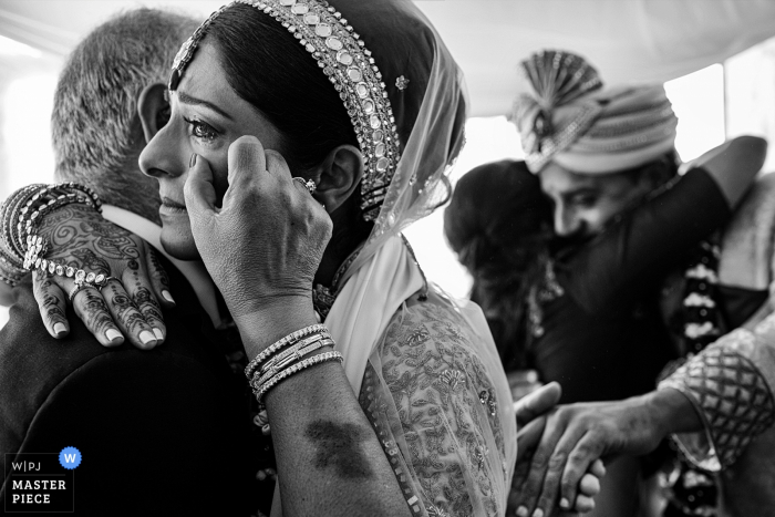 A bride wipes a tear from her eye as she embraces her father in this black and white photo as captured by Madrid wedding photographer 