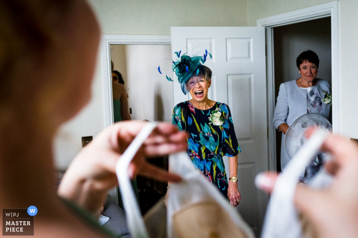 Hertfordshire wedding photographer captured this image of the brides mother in a blue fascinator hat seeing the dress for the first time