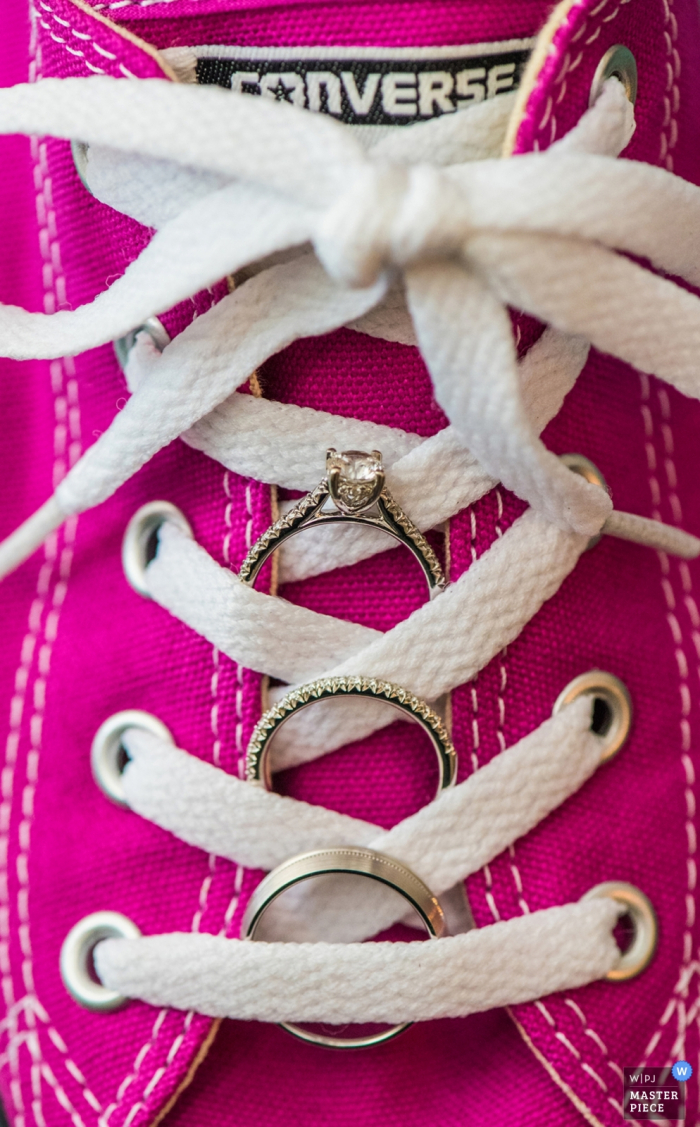 Este tiro de detalhe dos anéis de casamento aninhado entre os laços de sapatos de tênis converse rosa quente foi capturado por um fotógrafo de casamento de Charlotte