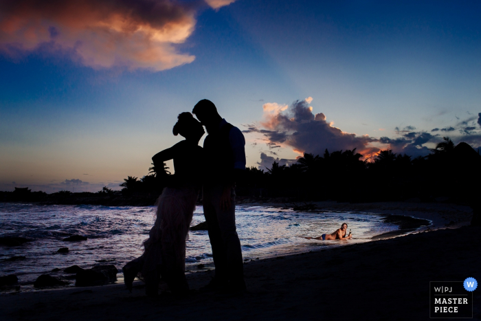 De bruid en bruidegom worden gesilhouetteerd op een strand terwijl ze kussen op deze foto door een Playa del Carmen.