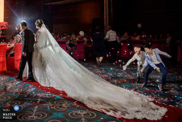 Photo by: <a href="https://www.wpja.com/contests/2017-tri3-photography-competition/kids-being-kids/2067941">Minifeel Lu - Taiwan</a> Photo of two young boys throwing flower petals as the bride's long train passes by a Taipei, Taiwan wedding photographer.