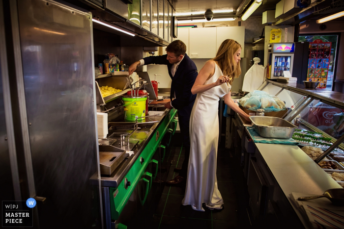 Photo by: <a href="https://www.wpja.com/contests/2017-tri3-photography-competition/food-drinks/2110746">Damon Pijlman - Netherlands</a> The bride and groom work in a kitchen in their wedding clothes in this photo by a Holland, Netherlands wedding photographer.