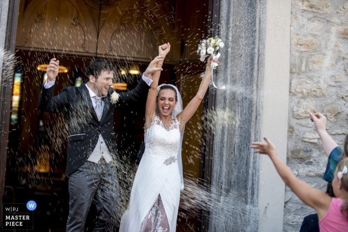 Foto door: <a href="https://www.wpja.com/contests/2017-tri3-photography-competition/ceremony/2089436"> Luigi Rota - Italië </a> De bruid en bruidegom heffen hun armen op tijdens de viering terwijl ze de ceremonie verlaten en gasten gooien rijst in deze foto door een huwelijksfotograaf uit Lombardije.