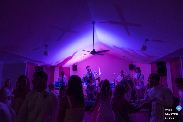 Photo by: <a href="https://www.wpja.com/contests/2017-tri3-photography-competition/musicians-djs/2078751">Dean Dampney - Australia</a> Musicians play on a stage as guests dance in blue and purple light in this photo by a New South Whales, Australia wedding photographer.