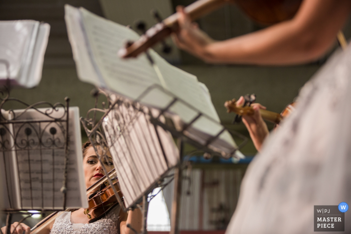Women sit in front of music stands as they play violins in this photo from Venice Women sit in front of music stands as they play violins in this photo by a Venice wedding photographer.