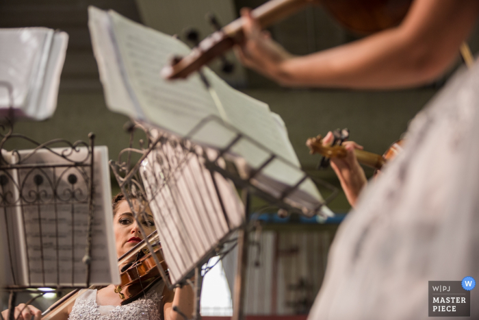 As mulheres sentam em frente a estantes de música enquanto tocam violinos nesta foto por um fotógrafo de casamento de Veneza.