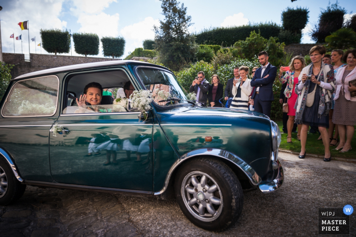 The bride waves to the guests from inside a small, green car in this send-off photo by a Morbihan wedding photographer.