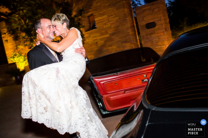 Le marié transporte la mariée jusqu'à une voiture sur cette photo prise par un photographe de mariage de l'Arizona.