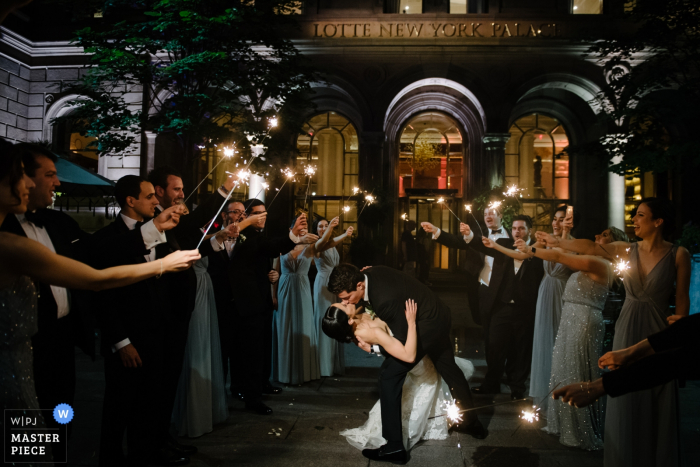 Auf diesem Foto eines Hochzeitsfotografen aus Manhattan, NY, küsst der Bräutigam seine Braut, während die Gäste auf beiden Seiten Wunderkerzen halten.