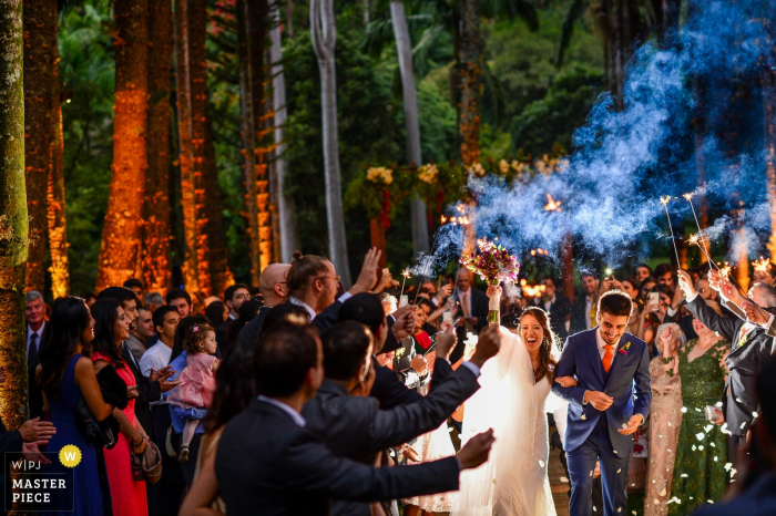 Foto della sposa e dello sposo che escono dalla cerimonia all'aperto attraverso gli ospiti che tengono le stelle filanti e che lanciano petali da un fotografo di matrimoni di San Paolo, in Brasile.