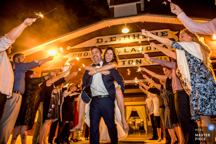 Photo of the bride riding on the groom's back as they exit the ceremony through guests holding sparklers by a Charlotte, NC wedding photographer.