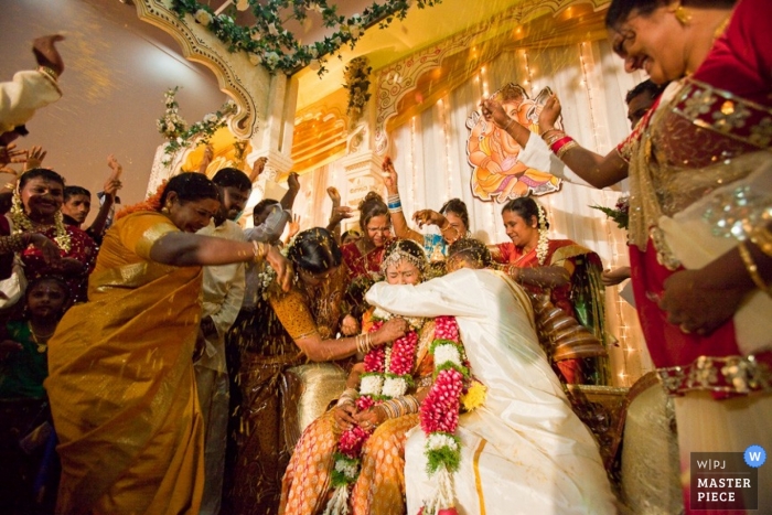 The beautiful bride and groom smiled radiantly as their saris glimmered in the vibrant lighting, amidst their family and guests The bride and groom smiled in delight surrounded by family, friends, and guests in beautiful saris at their wedding in Kuala Lumpur, captured perfectly in the warm lighting and adorned with bellowing bangles