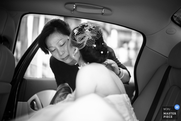 Un photographe de mariage a pris cette photo en noir et blanc de la mariée embrassant sa mère sur la joue avant le départ de la voiture pour se rendre à la cérémonie.