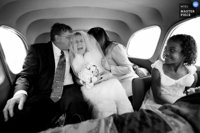 Un photographe de mariage à Paris a capturé cette joyeuse photo en noir et blanc de la mariée en train de rire pendant que son père l'embrasse sur la joue.