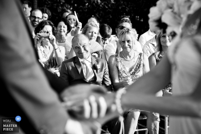 Phuket wedding photographer captured this black and white photo of the wedding guests in the background as the bride and grooms clasped hands are out of focus in the foreground