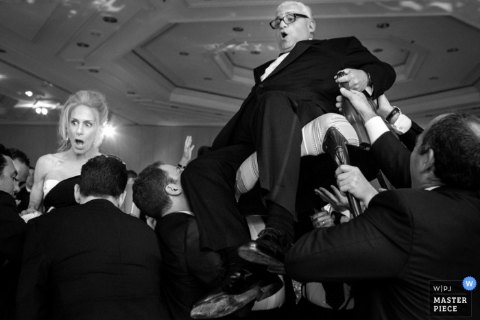 Photo de: <a href="https://www.wpja.com/contests/2013-q1-contest/parents/1155296"> Brett Butterstein - États-Unis </a> Le photographe de mariage de San Diego a capturé cette photo en noir et blanc de la mariée et du marié qui se font hisser sur des chaises au-dessus de la piste de danse