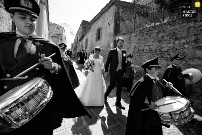 Photo by: <a href="https://www.wpja.com/contests/2013-q1-contest/full-frame-black-and-white/1144001">Danilo Coluccio - Italy</a> Reggio Calabria wedding photos of the bride and groom walking down the street with a marching band
