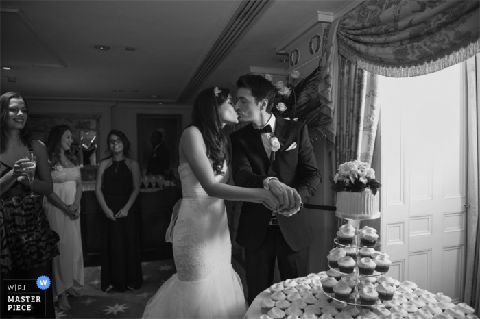 Photo by: <a href="https://www.wpja.com/contests/2013-q1-contest/full-frame-black-and-white/1150461">Marianne Earthy - United Kingdom</a> London wedding reportage photography - England black and white photo of the bride and groom kissing before cutting the cake