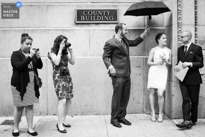 Photo: <a href="https://www.wpja.com/contests/2013-q3-contest/ceremony/1246551"> Allison Williams - États-Unis </a> Photographe de mariage de Chicago | L'image contient: marié, mariée, noir et blanc, bâtiment, parapluie, femmes, appareils photo