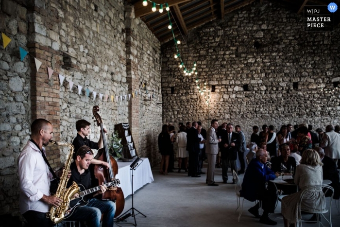 Fotografia di matrimonio nel Morbihan | L'immagine contiene: reception, edificio in pietra, castello, musicisti, sassofono, violoncello, chitarra, ospiti