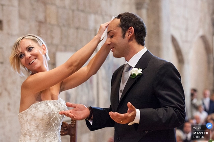 Photo by: <a href="https://www.wpja.com/contests/2014-q1-photography-contest/ceremony/1389111">Andrea Brucculeri - Italy</a> Rome Wedding Photographer | Image contains: bride wiping sweat from groom's brow during ceremony