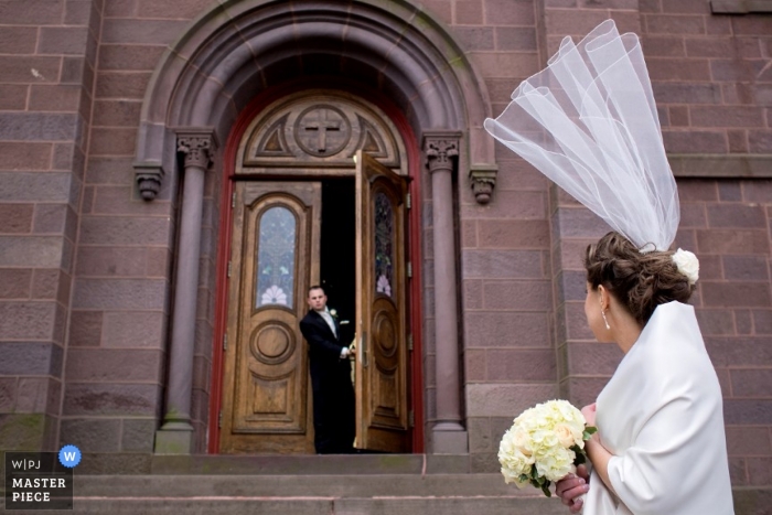 Photo by: <a href="https://www.wpja.com/contests/2014-q1-photography-contest/ceremony/1407476">Joe Brier - United States</a> Massachusetts bride has veil flying away, upward outside of church.