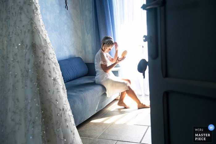 Photo by: <a href="https://www.wpja.com/contests/2014-q1-photography-contest/getting-ready/1389086">Andrea Brucculeri - Italy</a> Wedding photograph from Rome | Image contains: getting ready, dress, light, door, blue, couch, bride