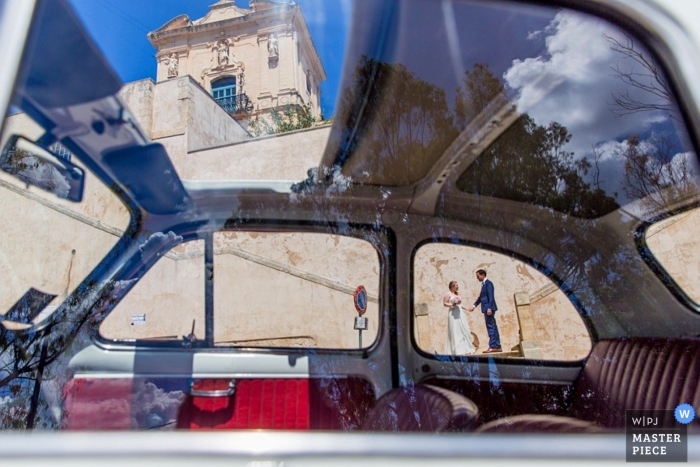 Peering through a car window under blue skies, a wedding couple stand outside in Zuid Holland photo