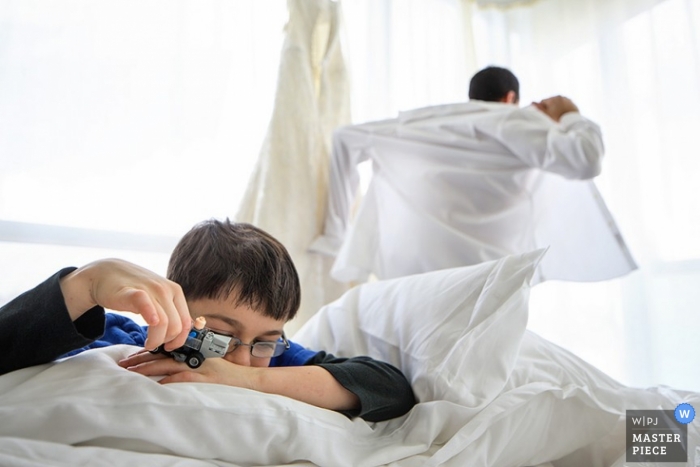 Image of a New York City groom putting on his shirt near the window as he prepares for his wedding ceremony