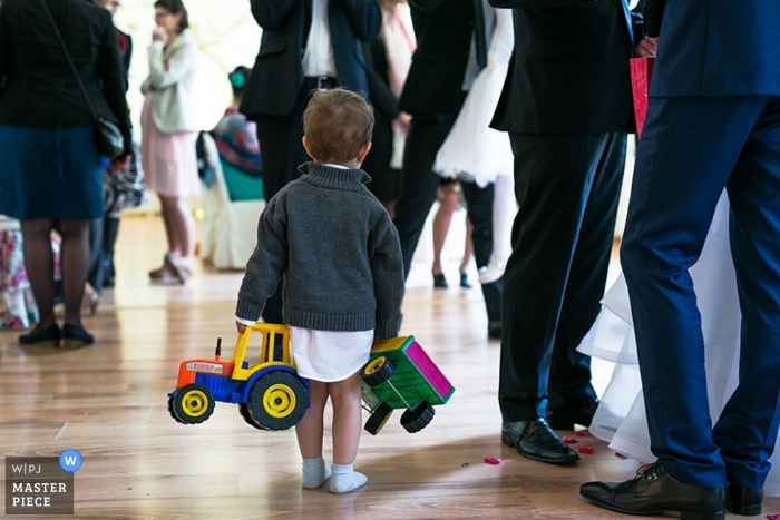 An image from Lower Silesian of a young boy clutching his tractor toys at an indoor wedding reception in Poland creates a pleasing contrast at a special celebration