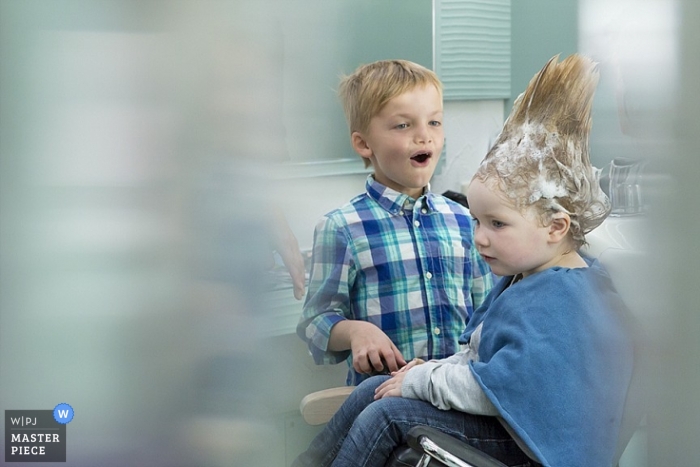 Irokesenschnitt für die Hochzeit eines Kleinen, der sich die Haare waschen lässt, bevor er sich auf die Hochzeitszeremonie vorbereitet, während ein verblüffter junger Freund in diesem süßen Badezimmer offen zuschaut