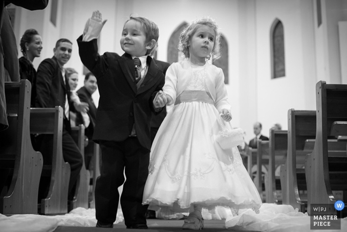 A black and white photo of a confident page boy, and uncertain flower girl as they walk down the aisle in Rio Grande do Sul, Brazil.