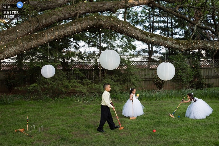 Le ragazze dei fiori e un ragazzo di pagina giocano a croquet su prato al di fuori di Philadelphia PA durante una pausa nelle feste di matrimonio