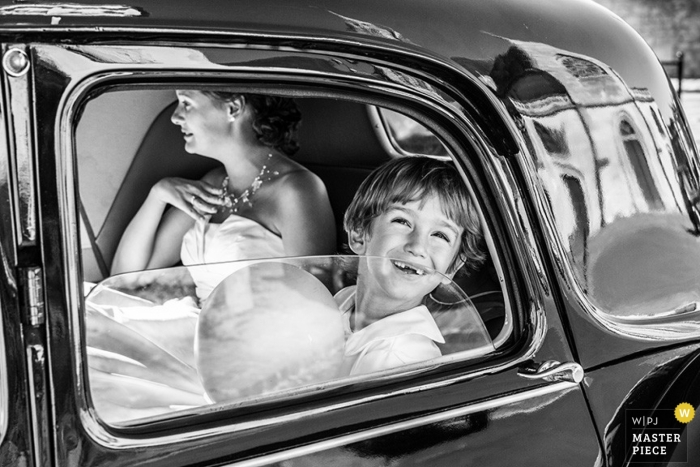 Black and white image of a Paris bride and child inside their vehicle with a reflection of the church on the paintwork