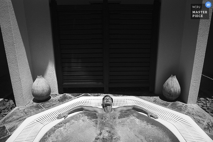 Un hombre relajándose en su enorme jacuzzi espumoso en una interesante toma de una fotografía de boda con enormes puertas de madera en el fondo en blanco y negro