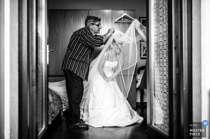 Modifiche dell'ultimo minuto al velo da sposa della sposa e lei si china per accogliere la sarta sulla soglia della sua suite