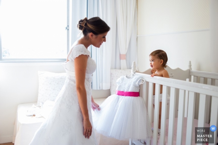 Au Brésil, une mariée de Bahia partage un regard avec sa fille dans la crèche, avant de l'aider à s'habiller d'une robe blanche bouffante avec un ruban rose