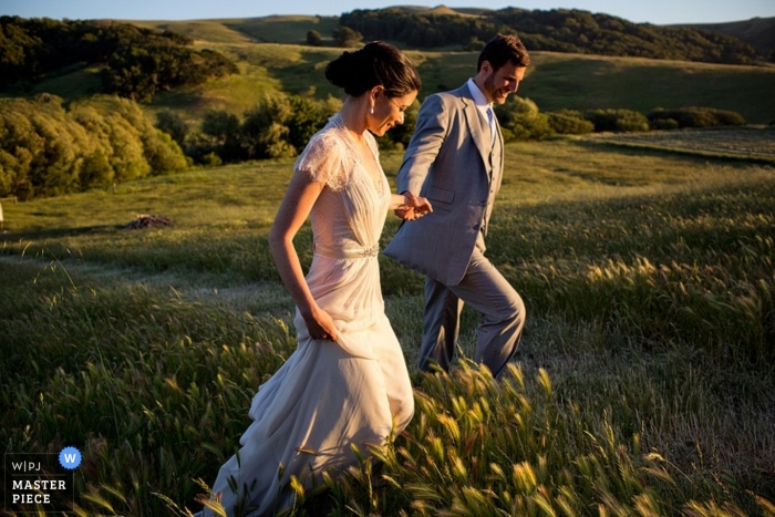 A bride and groom stroll hand in hand through field as photographed by a Bahamas wedding photographer